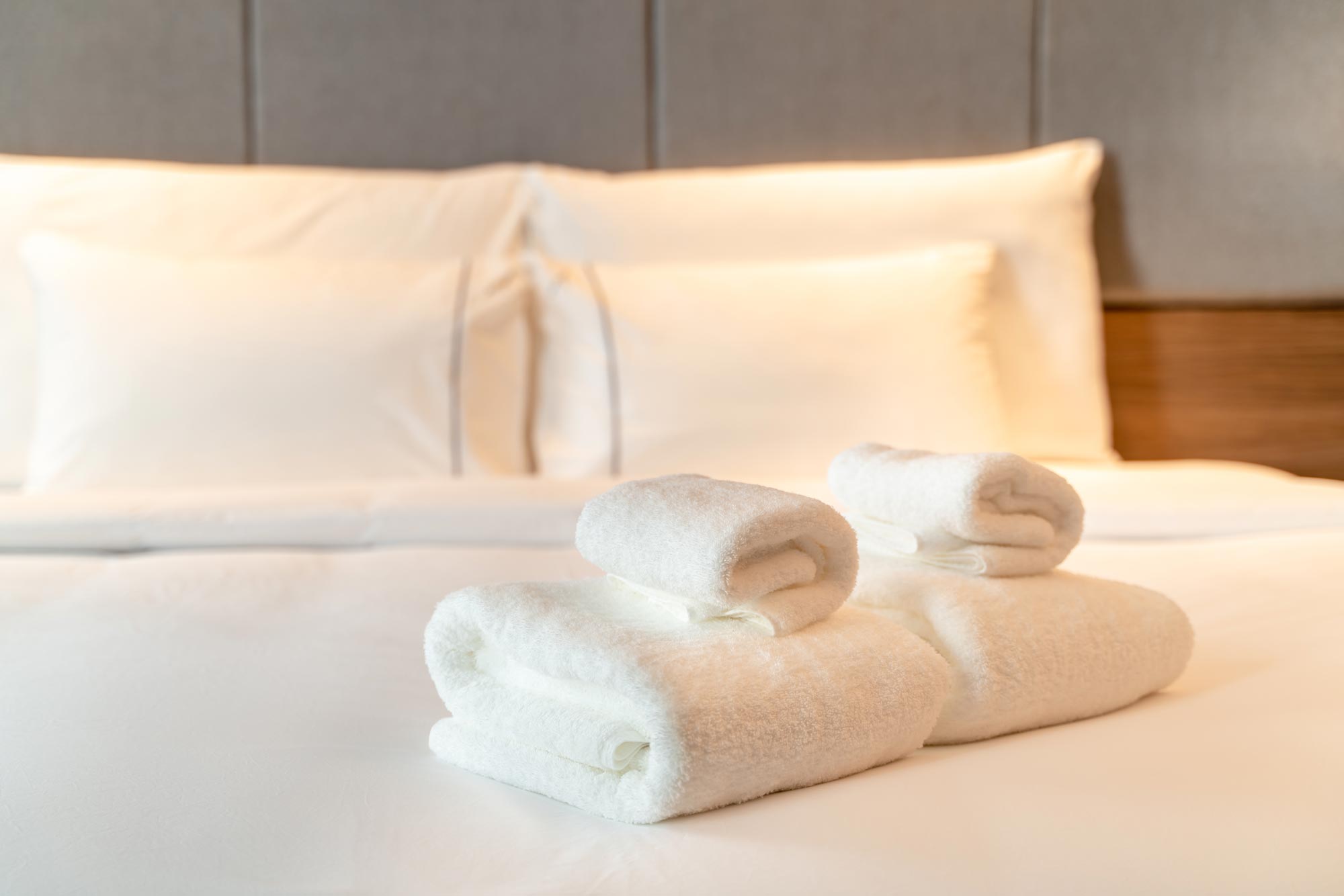 En närbildskomposition visar noggrant förberedda vita handdukar, både vikta och hoprullade, arrangeade på en hotellsäng med vita lakan och kuddar